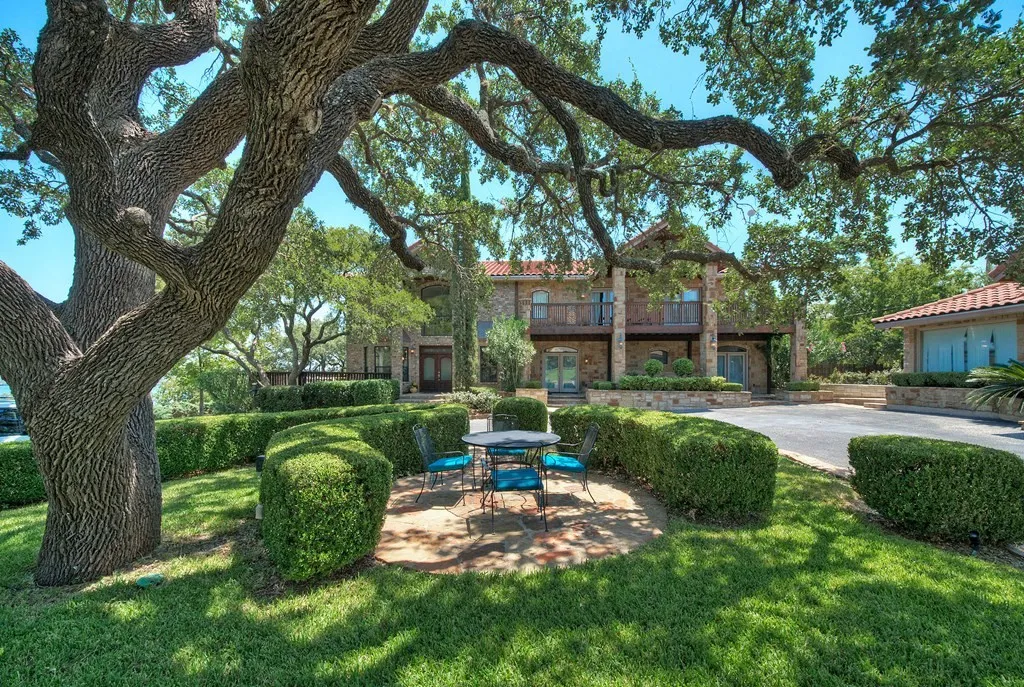 Patio table and blue-cushioned chairs under a sprawling oak, main house behind