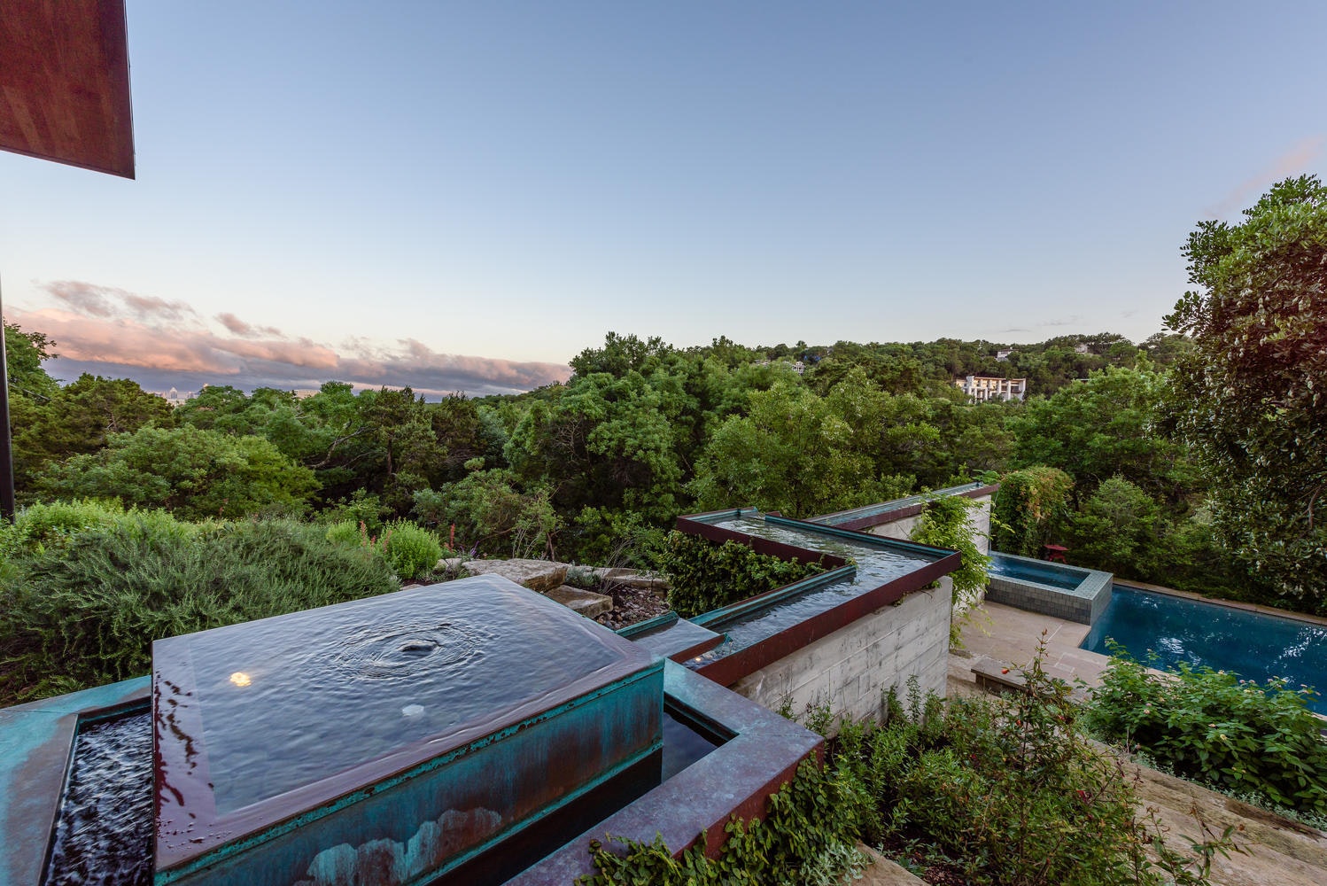 A copper water feature at dusk, with the pool and hillside view beyond